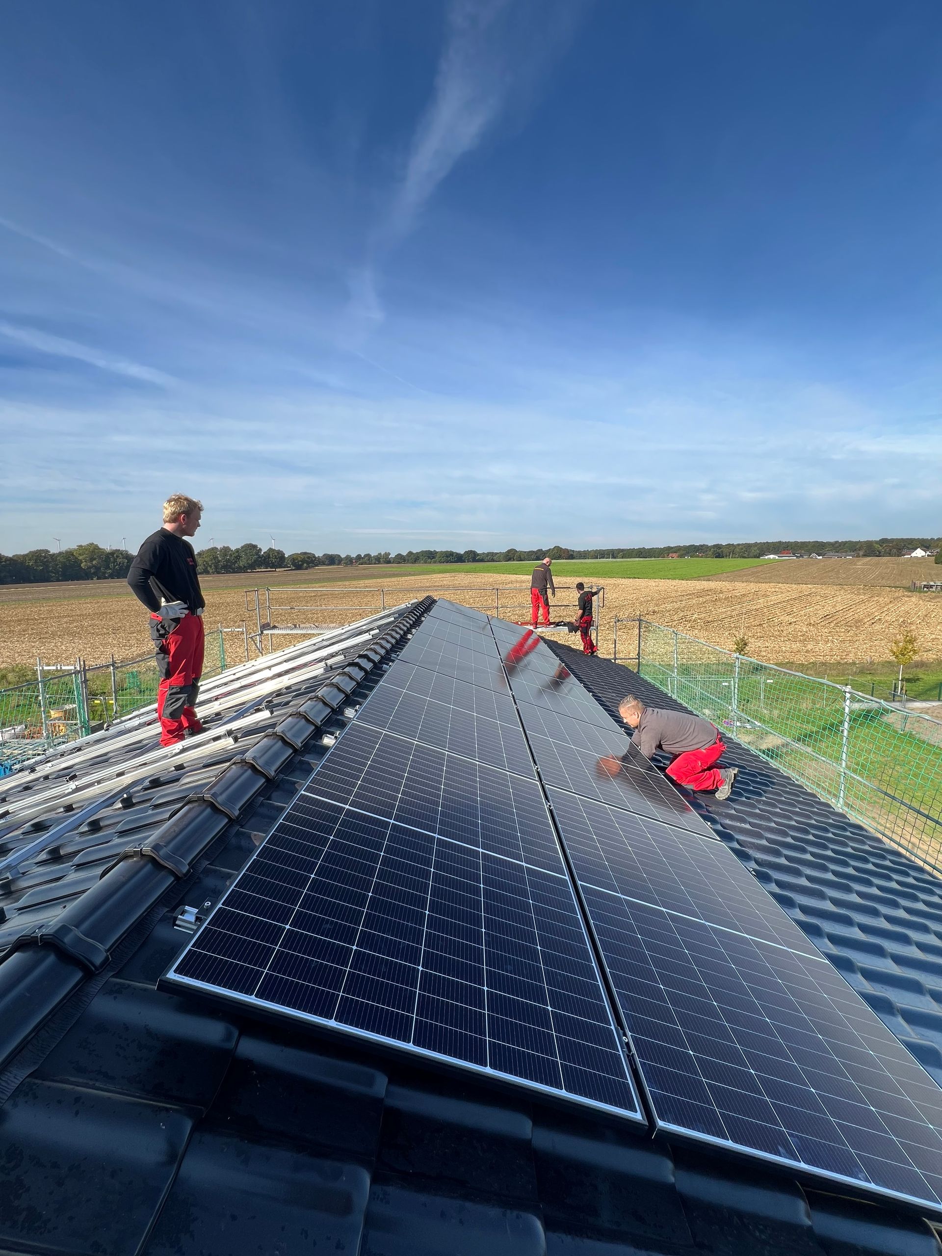 Arbeiter installieren Solarpaneele auf einem Dach unter blauem Himmel