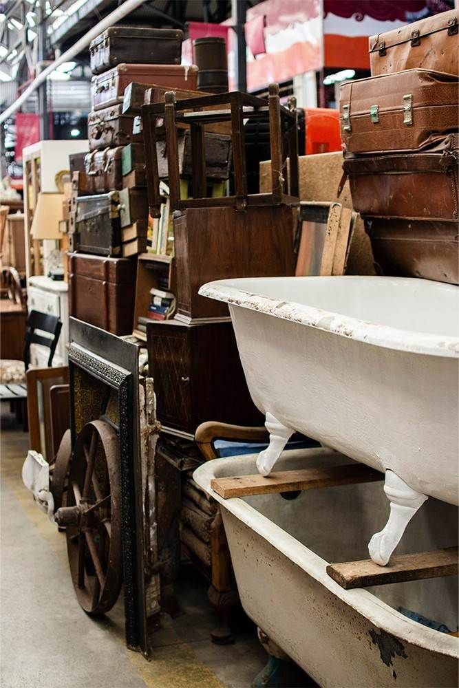 Un pasillo abarrotado de una tienda de antigüedades, con muebles viejos apilados y una bañera.