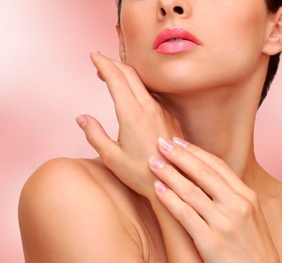 Primer plano del rostro y las manos de una persona con labios rosados brillantes sobre un fondo rosa suave.