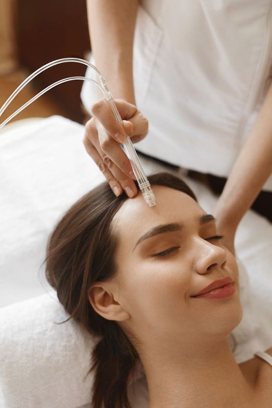 La persona que recibe un tratamiento facial, mientras el profesional sostiene un dispositivo de mano cerca de la frente.