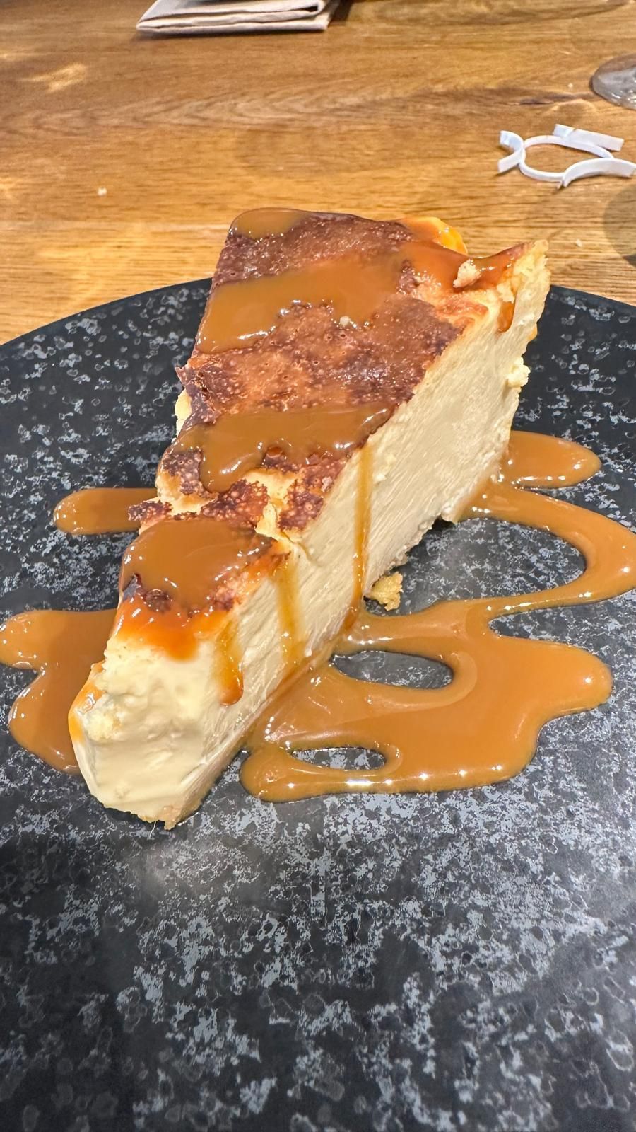 Una rebanada de tarta de queso con salsa de caramelo en un plato negro.