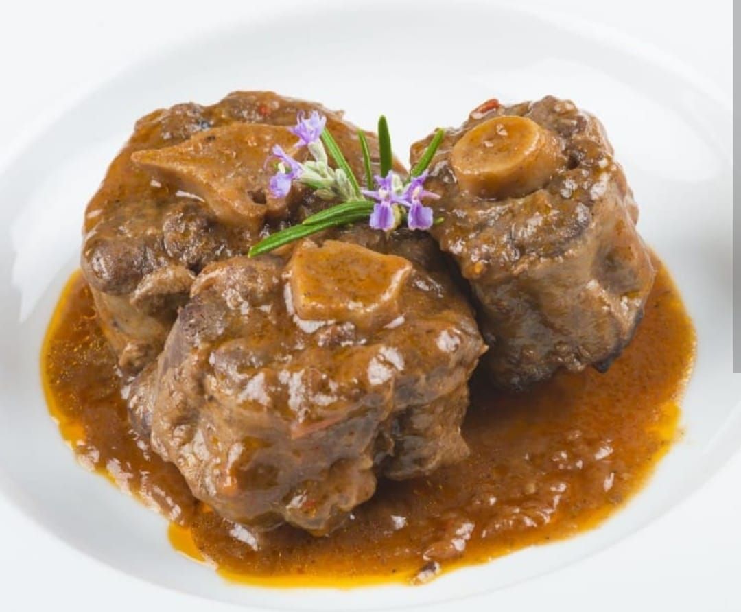 Un plato blanco cubierto con carne y salsa con flores moradas encima.