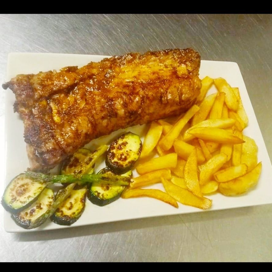 Un plato blanco cubierto con costillas y papas fritas.