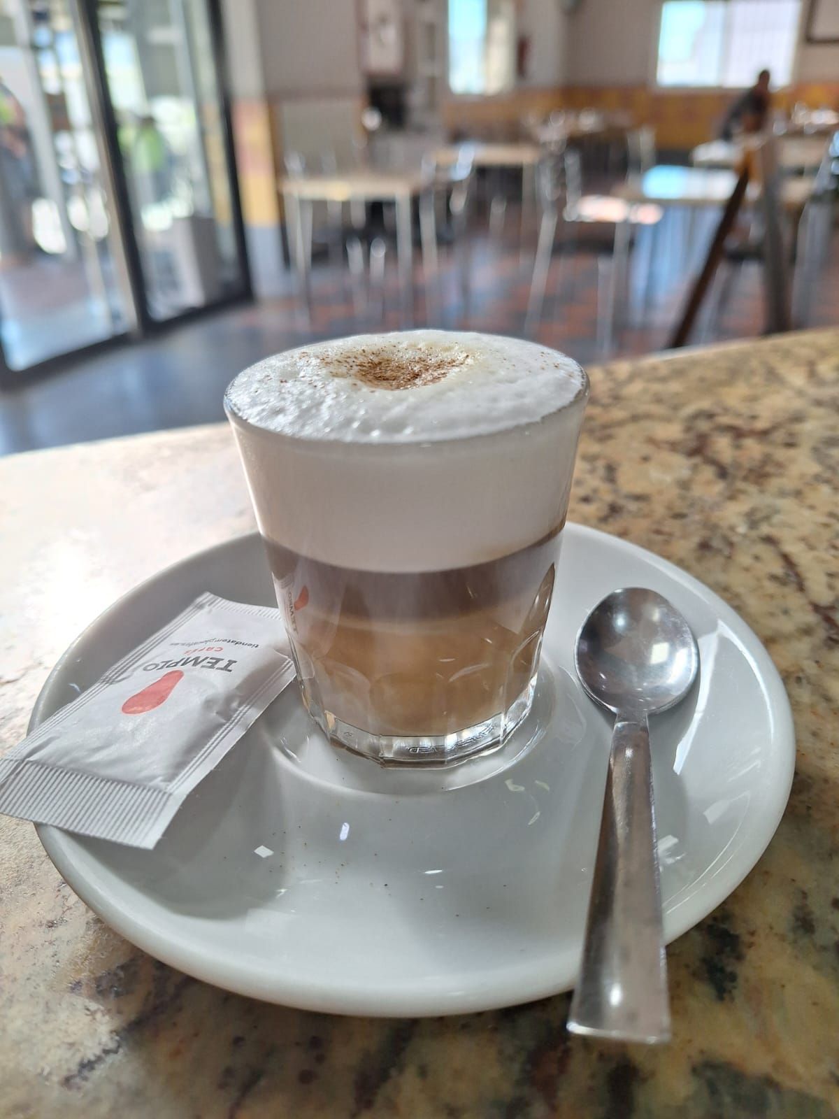 Una taza de capuchino en un platillo con una cuchara sobre una mesa.