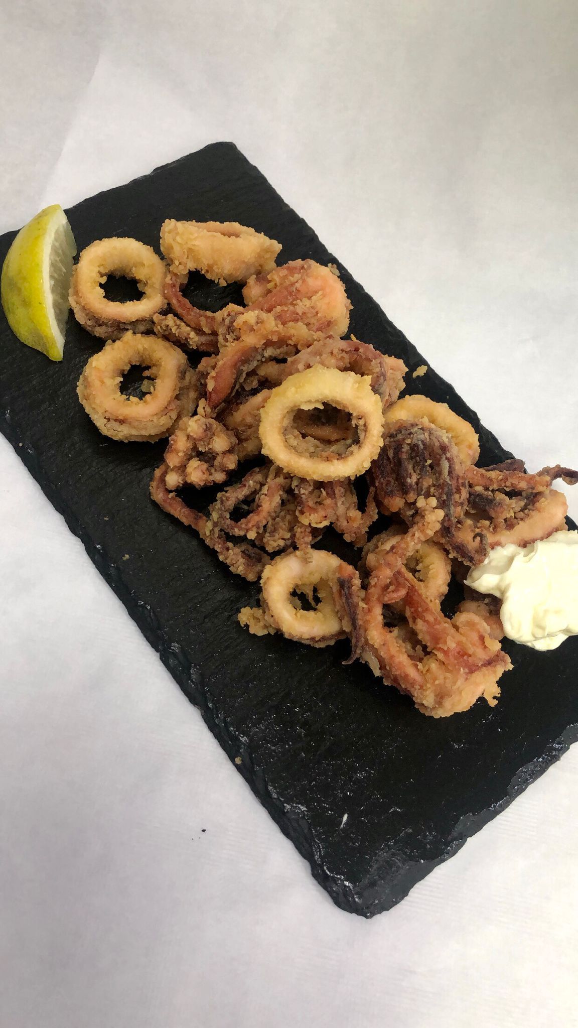 Un plato negro cubierto con anillos de calamar fritos y una rodaja de limón.