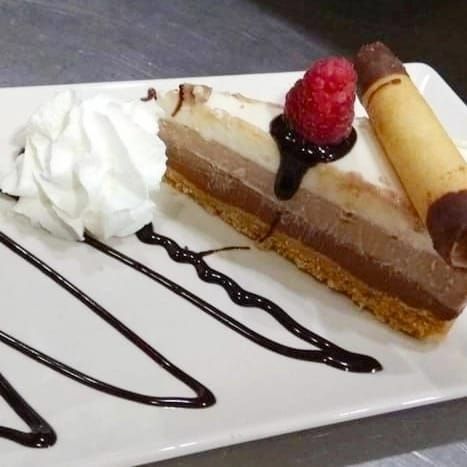 Un trozo de pastel de chocolate con crema batida y frambuesas en un plato blanco