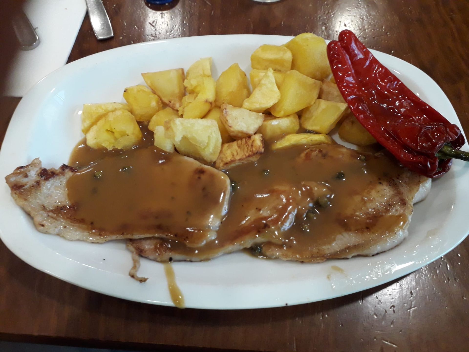 Un plato de comida con carne y patatas en una mesa.