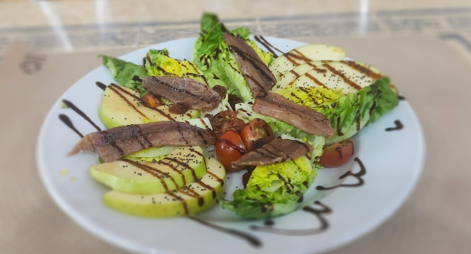 Un plato blanco cubierto con una ensalada de lechuga, tomates y anchoas.