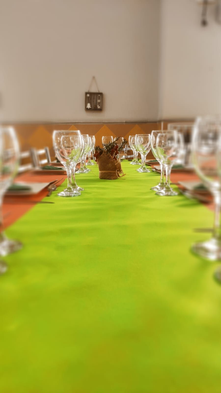 Una mesa larga con un camino de mesa verde y copas de vino sobre ella.