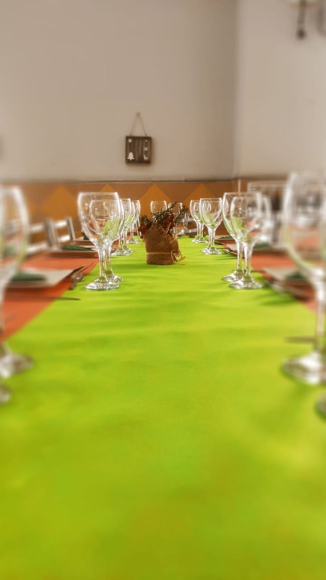 Una mesa larga con un camino de mesa verde y copas de vino sobre ella.