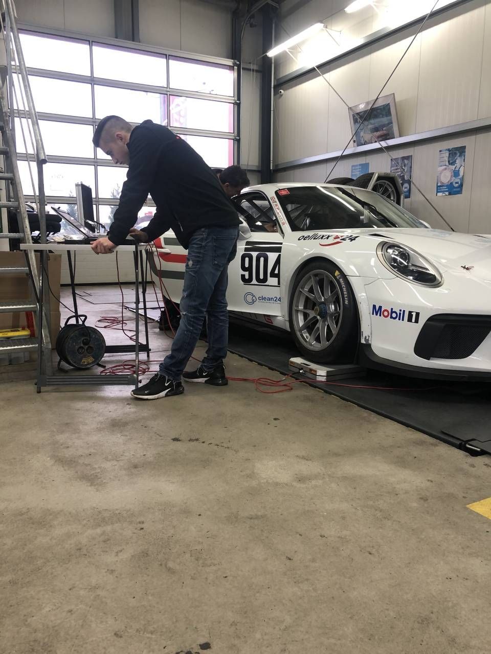 Person betrachtet etwas auf dem Laptop vor Rennauto in einer Werkstatt