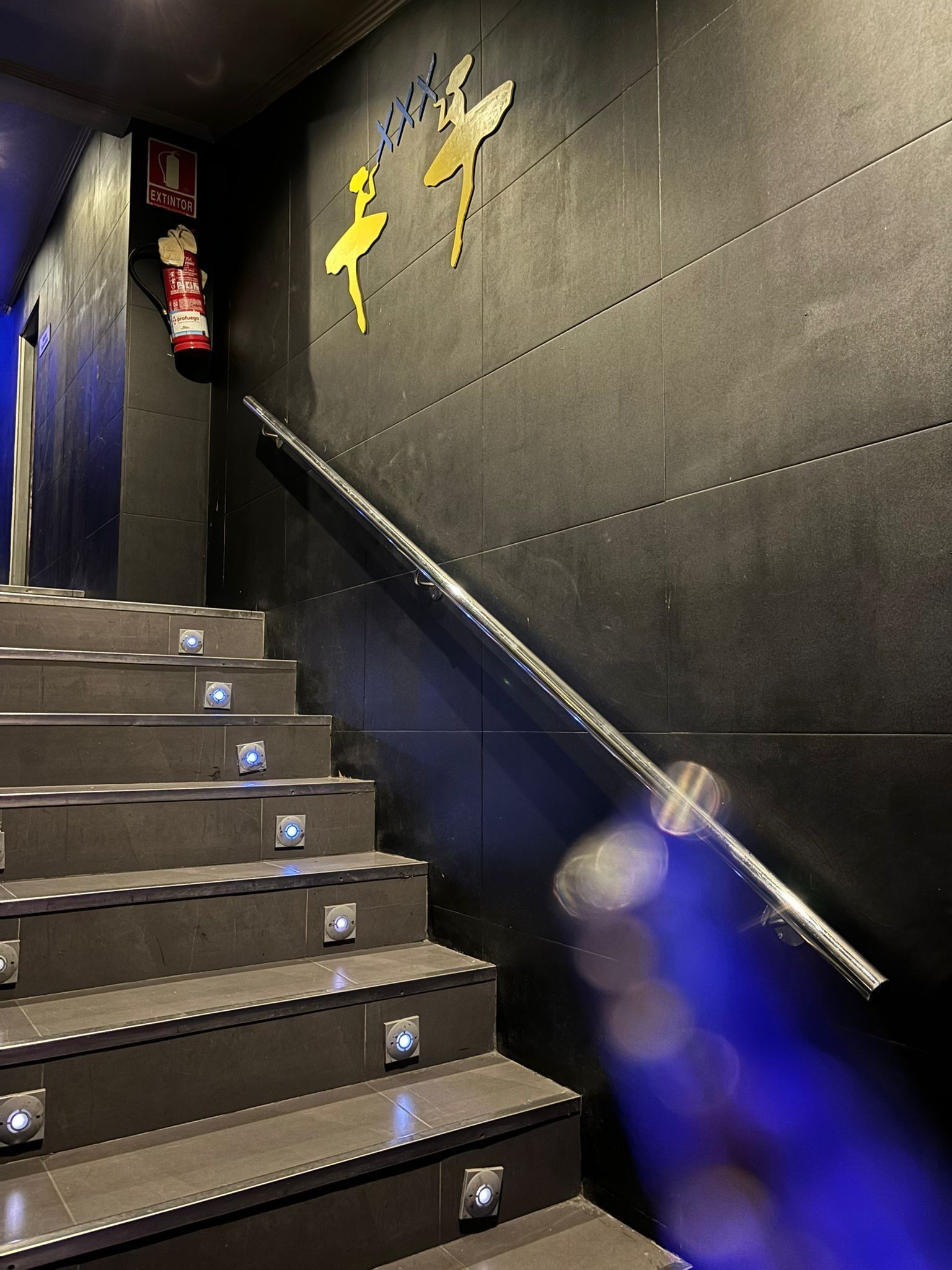 Una escalera con barandilla de metal y un extintor en la pared.