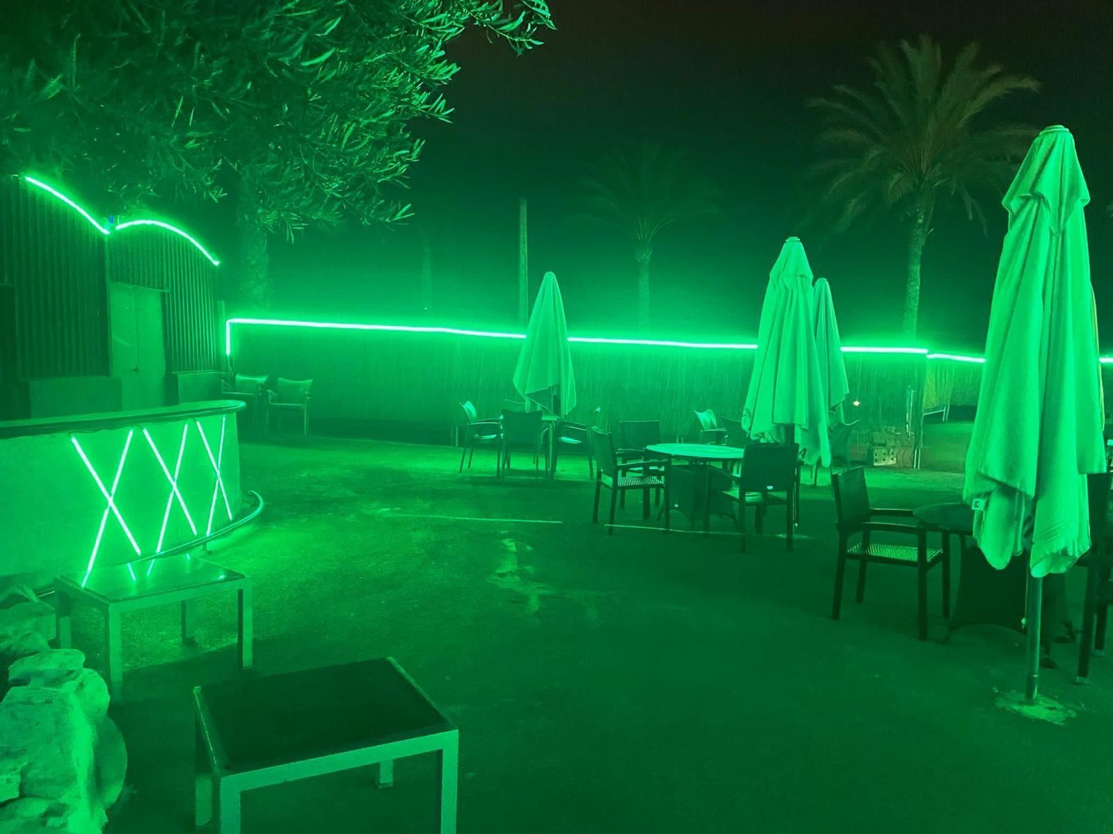 Un patio con mesas y sombrillas iluminado con luces verdes por la noche.