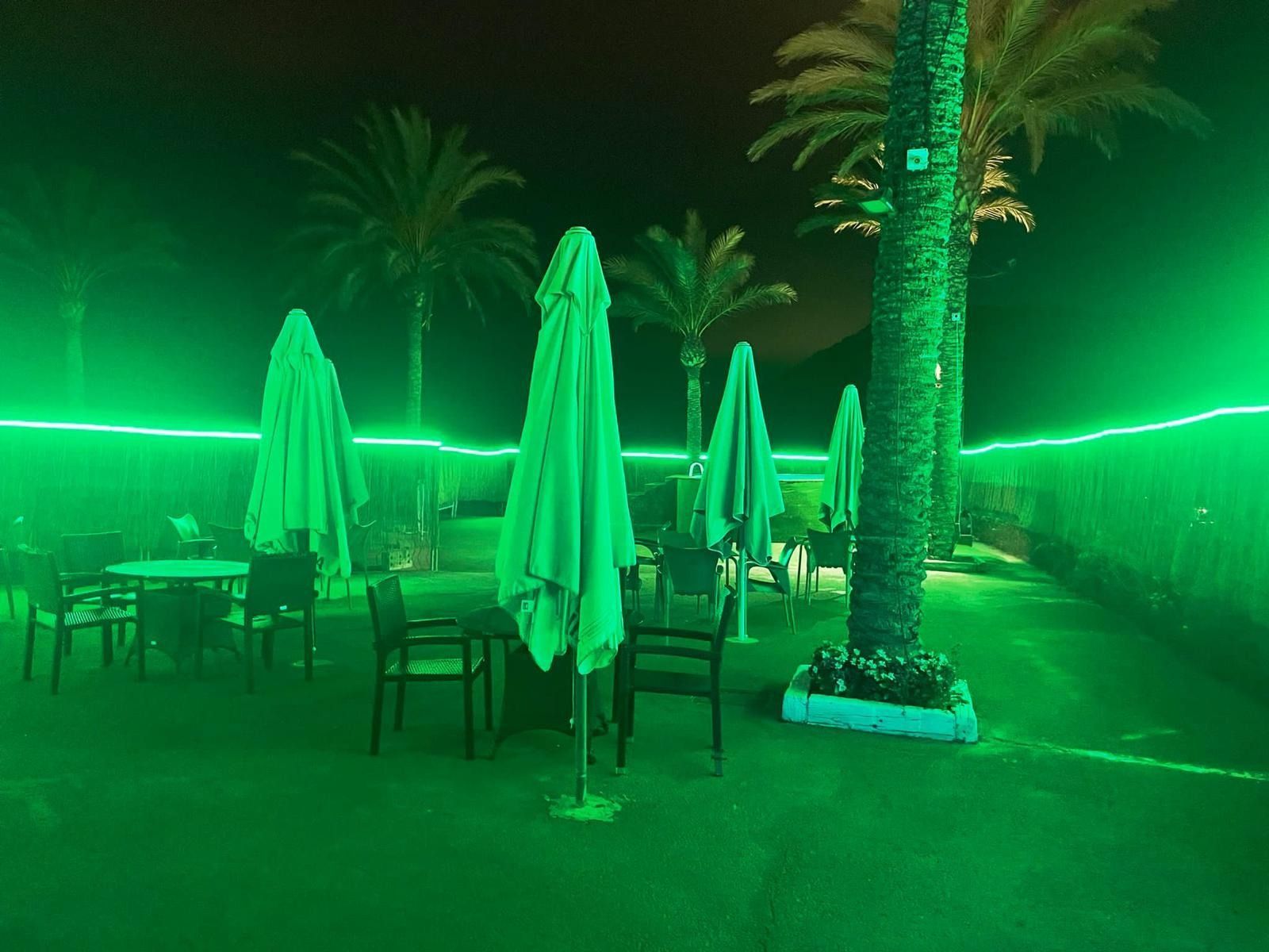 Una fila de mesas y sillas bajo luces verdes por la noche.