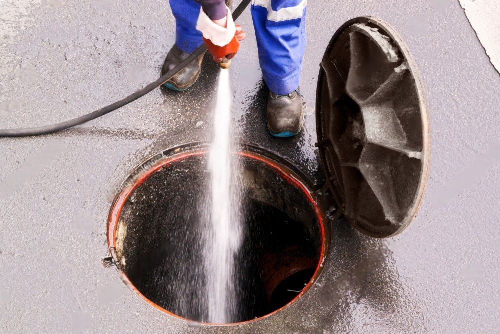 Person hält Wasserschlauch in Kanaldeckel