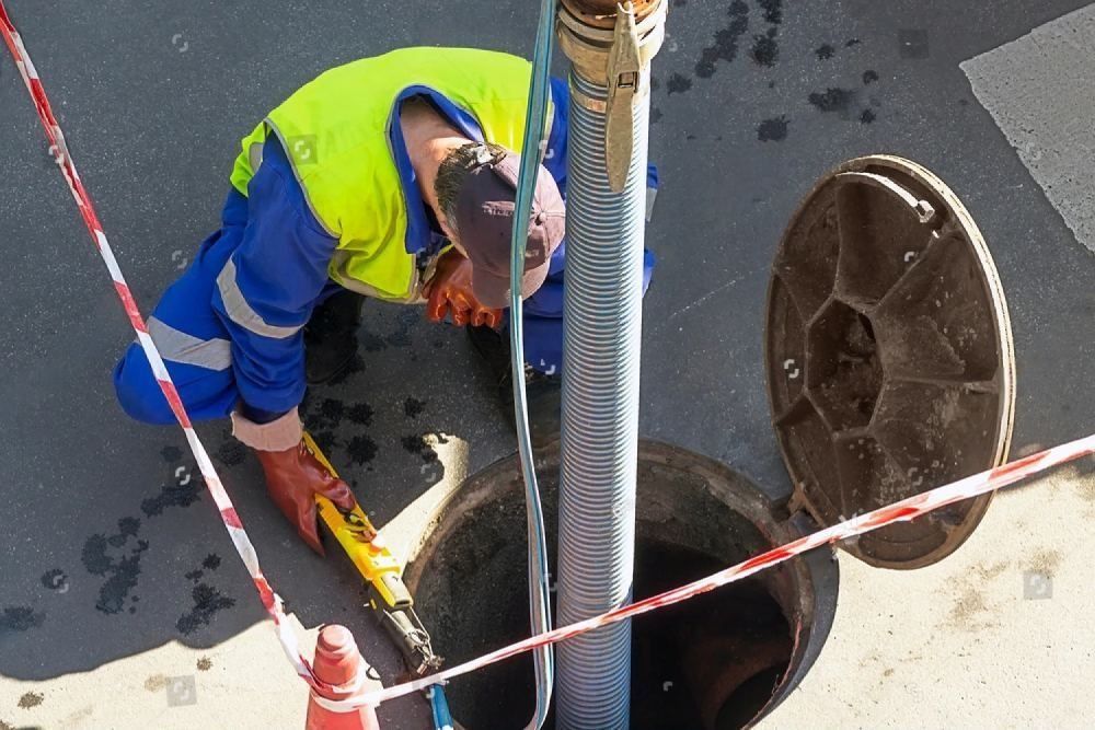 Perso kniet vor Kanaldeckel, Schlauch in Kanaldeckel