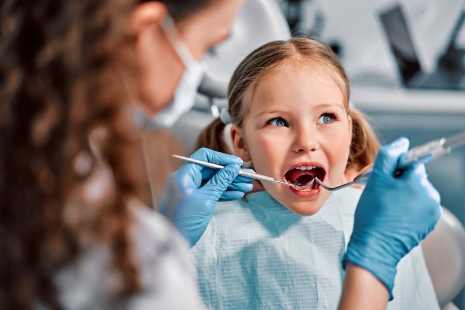 Une petite fille se fait examiner les dents par un dentiste.