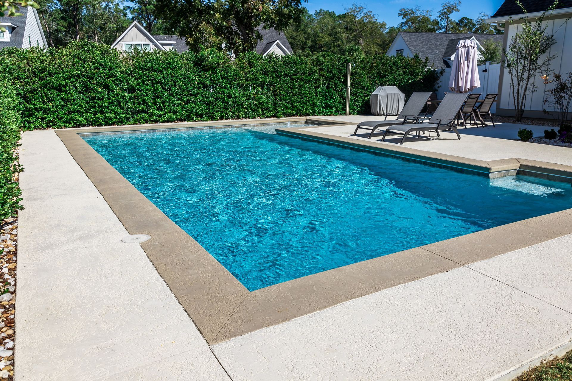 Piscine rectangulaire dans le jardin avec eau bleue, margelles beiges et chaises longues sur une terrasse ensoleillée