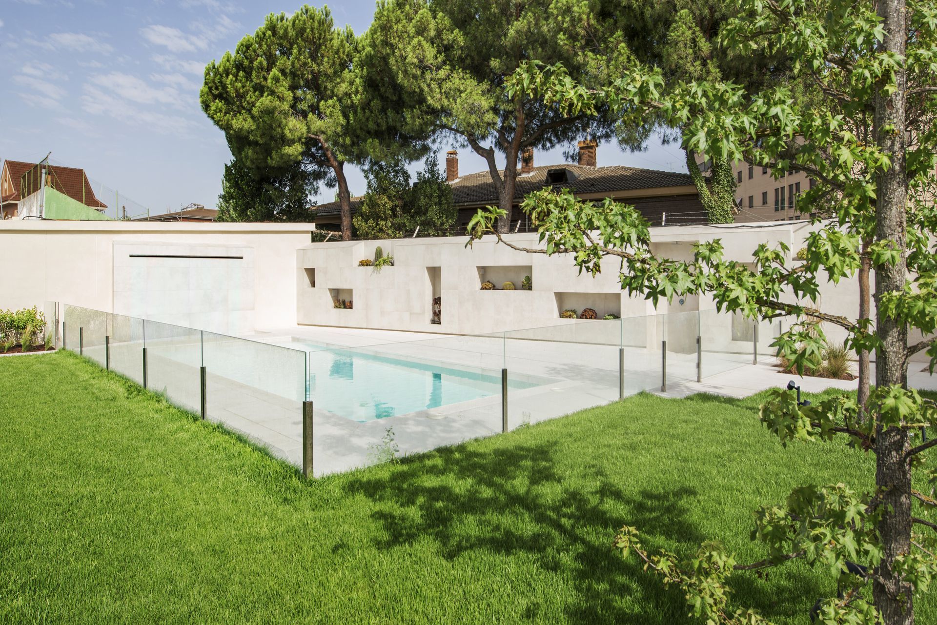 Maison blanche moderne avec piscine et pelouse verdoyante clôturées à l'arrière, sous les arbres.