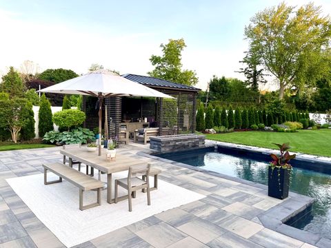Terrasse arrière avec table à manger, parasol, chaises longues et piscine entourée de verdure.