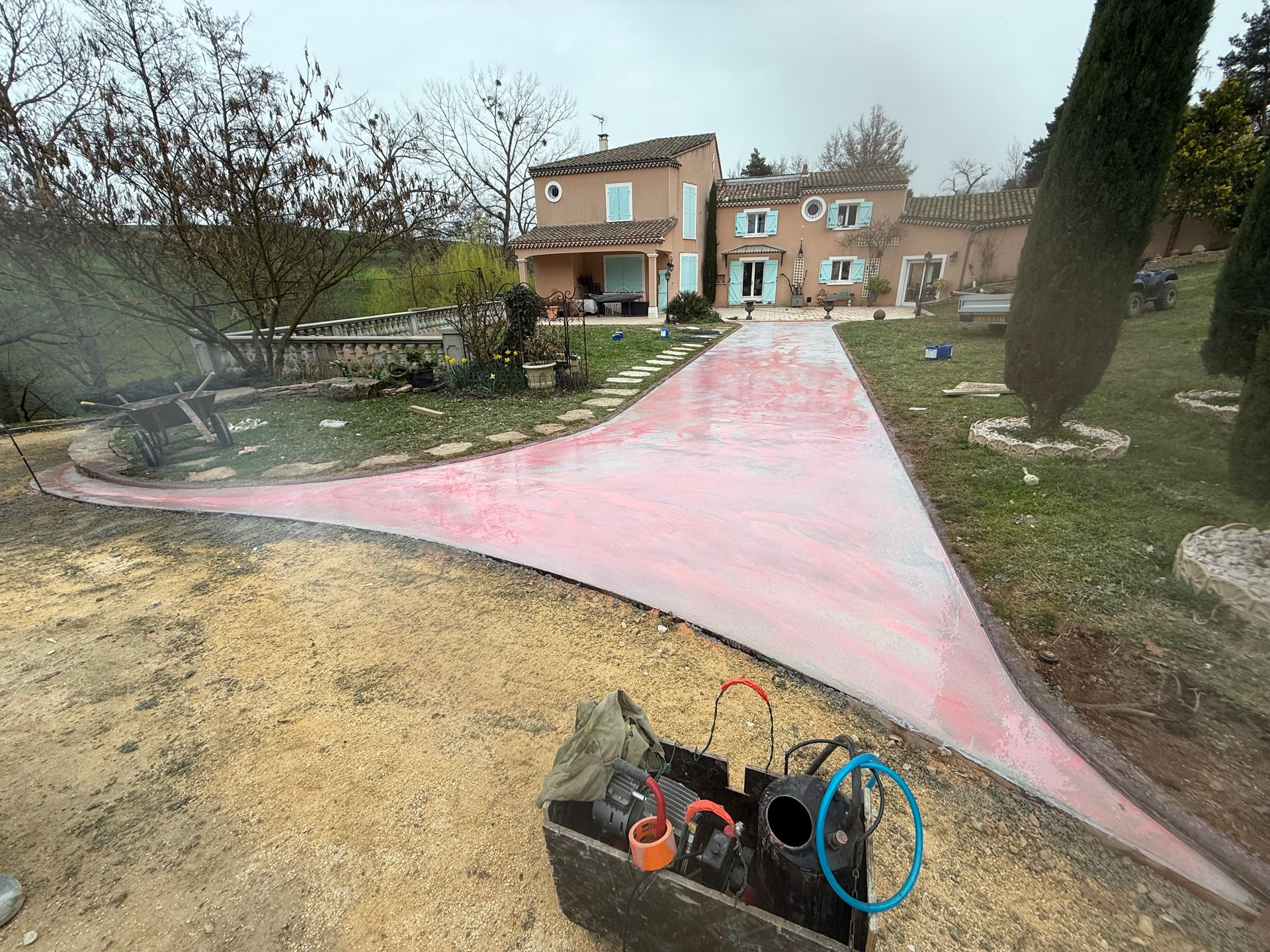 Allée rose menant à une maison dans une cour, avec des outils de jardinage au premier plan.