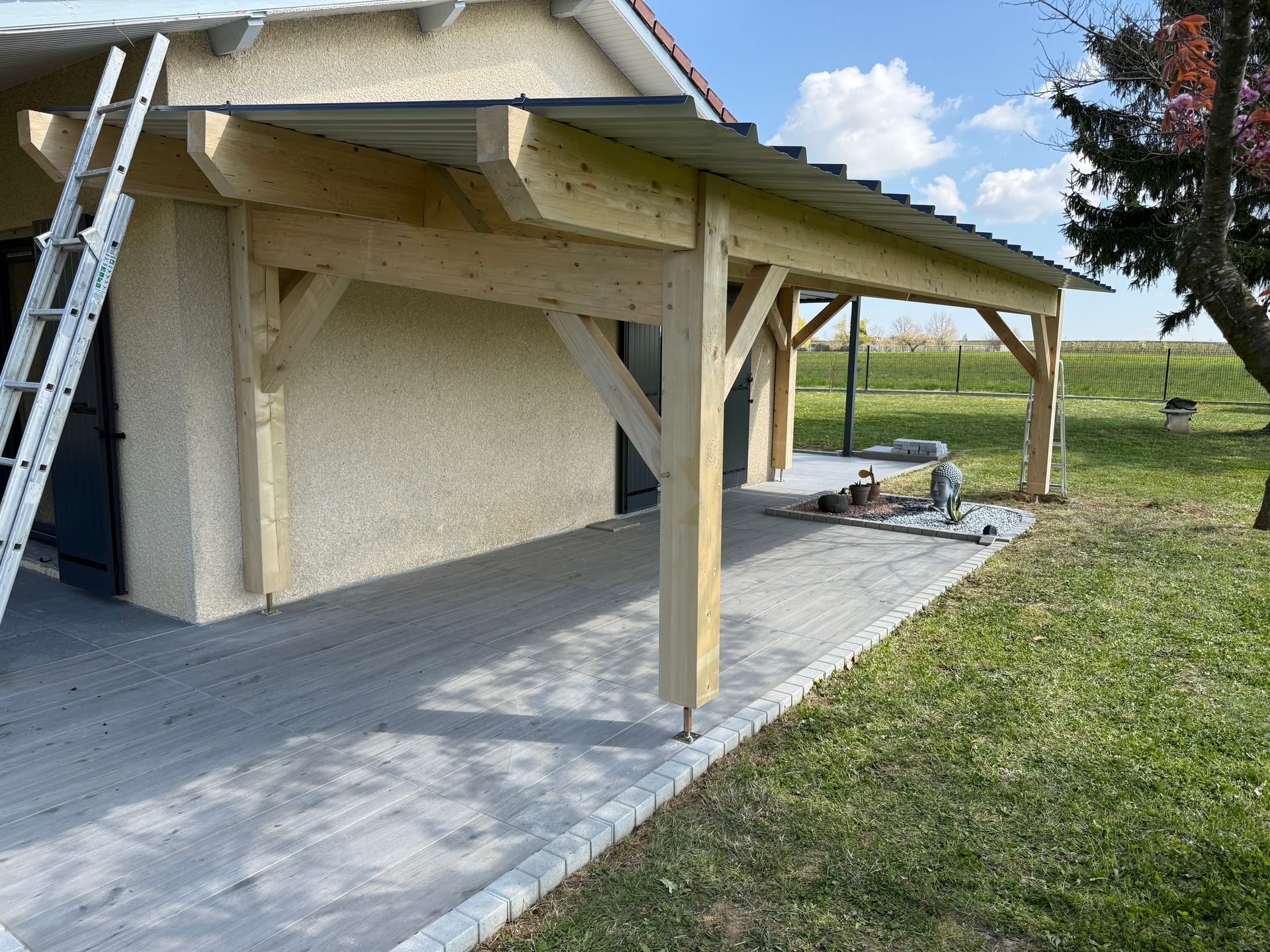Petite maison avec une véranda en bois couverte et une terrasse en béton dans une cour rurale