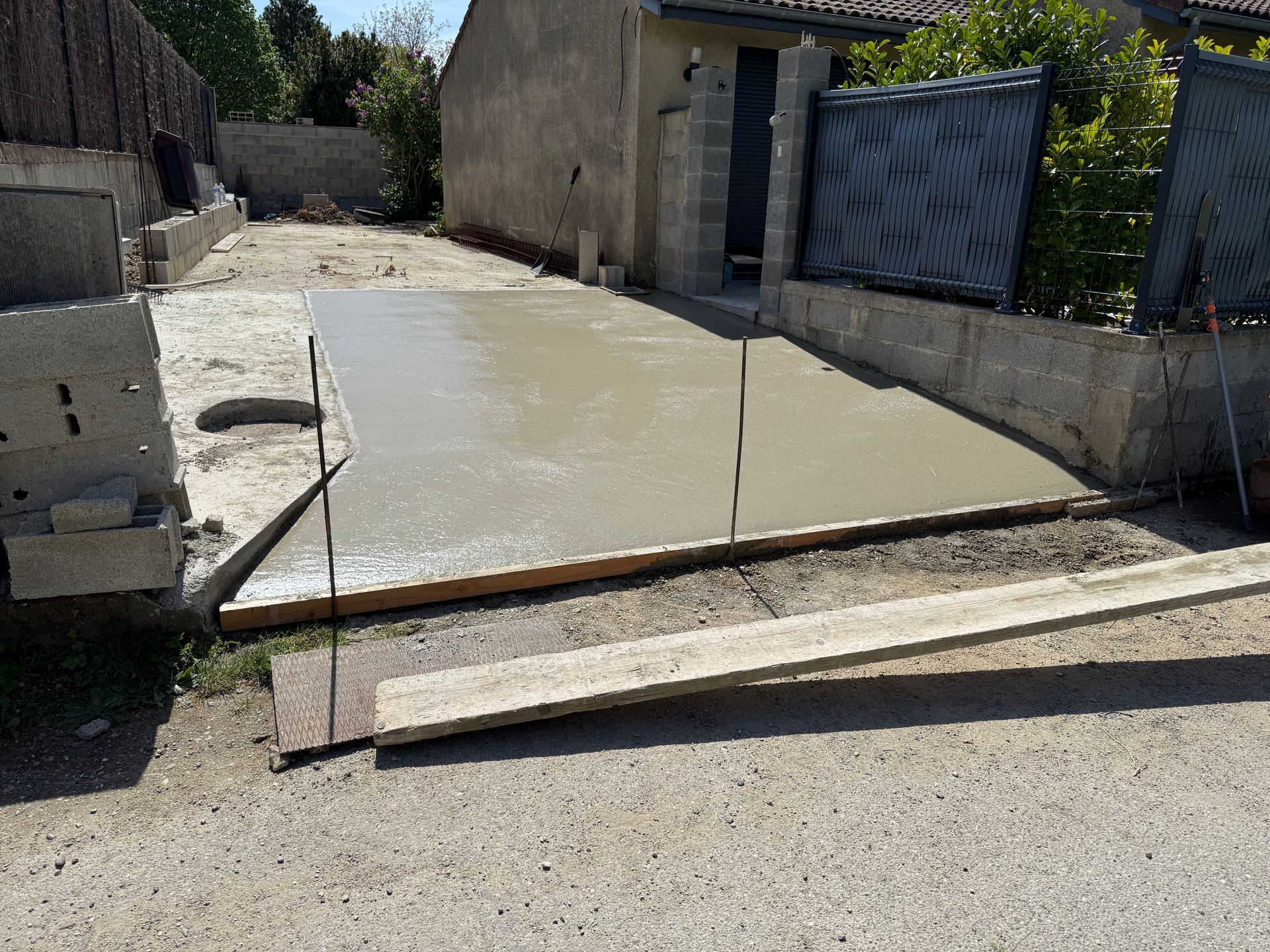 Allée en béton avec une légère pente, un trottoir bas et un portail métallique à côté d'un garage.