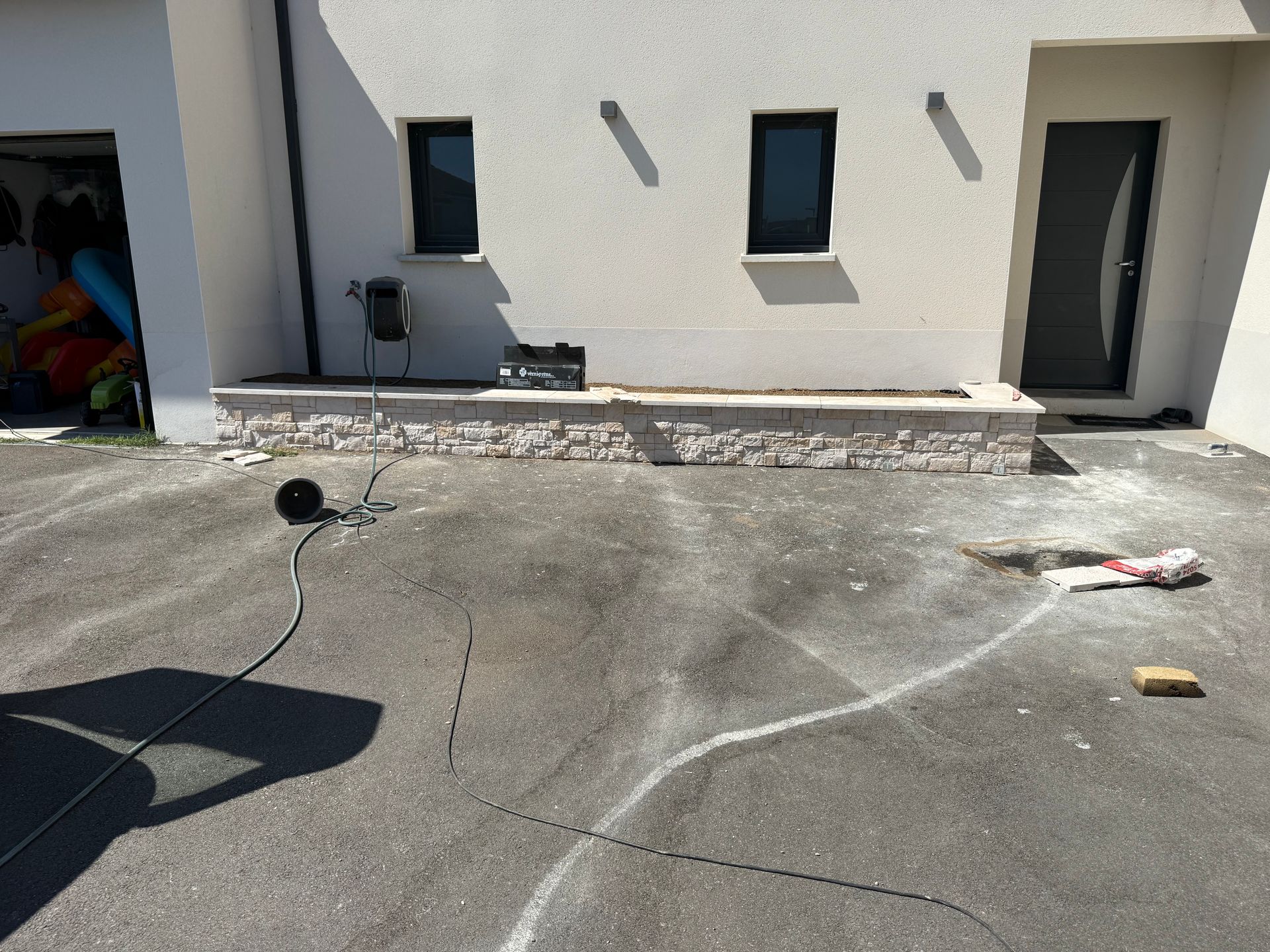 Cour en béton jouxtant un bâtiment blanc, avec des tuyaux d'arrosage et des débris éparpillés au sol.