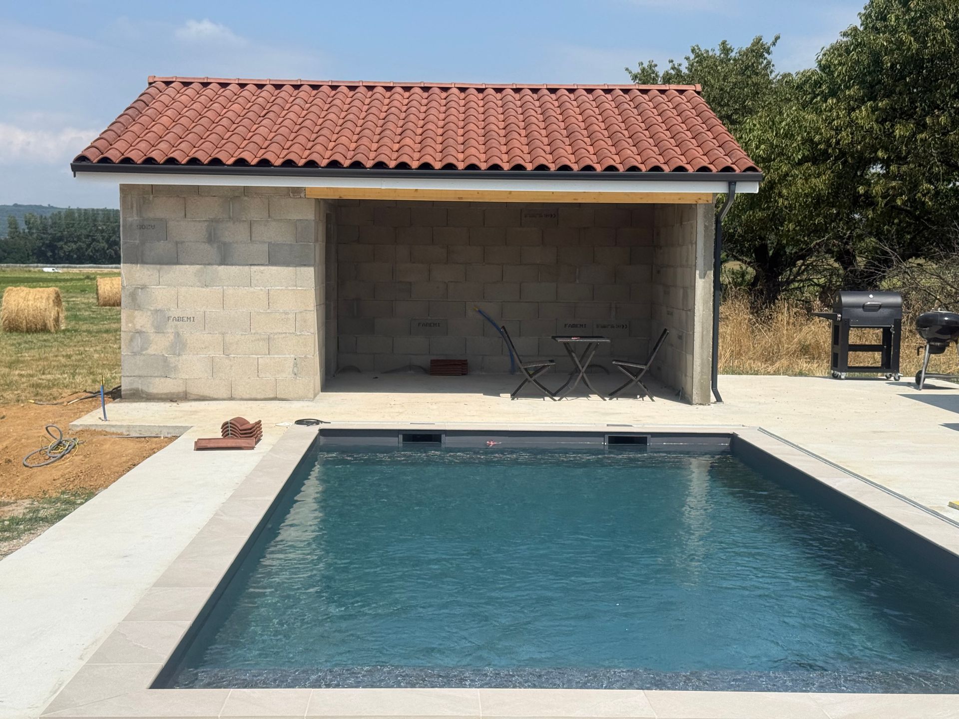 Piscine dans le jardin à côté d'un cabanon en pierre au toit de tuiles rouges par une journée ensoleillée