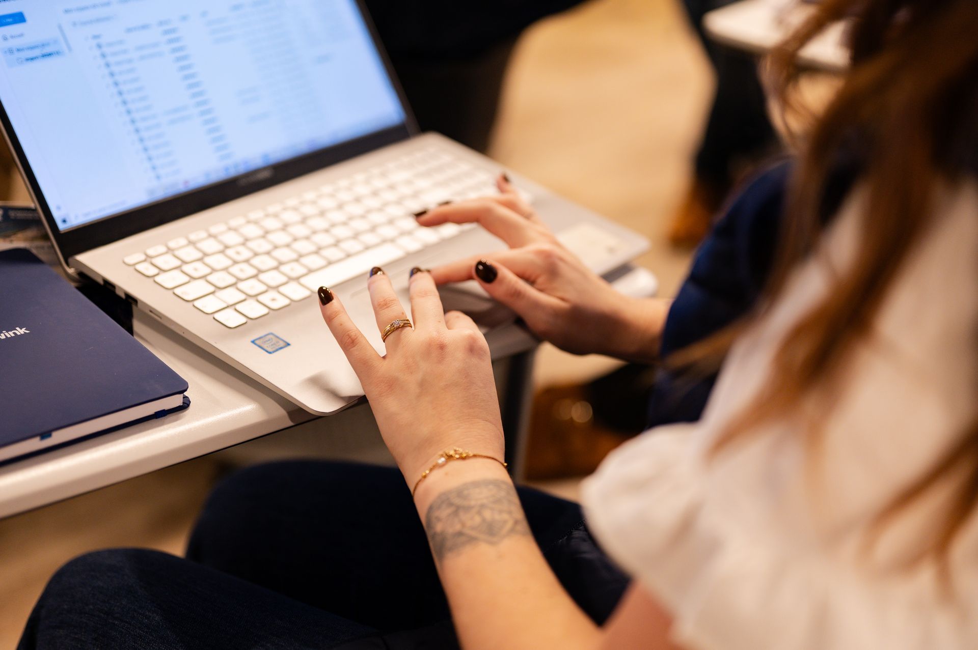 Gros plan sur des mains portant des bagues et un bracelet, tapant sur le clavier d'un ordinateur portable à côté d'un carnet.