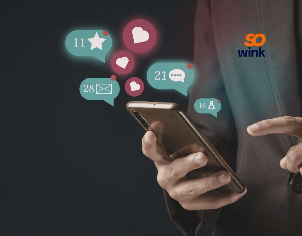 Une personne utilise un ordinateur portable et un smartphone avec des émojis et des icônes de réseaux sociaux qui tourbillonnent autour.