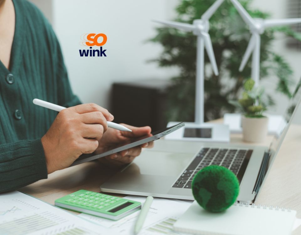 Une personne utilisant un stylet sur une tablette, assise à un bureau avec un ordinateur portable, une calculatrice et une maquette d'éolienne.