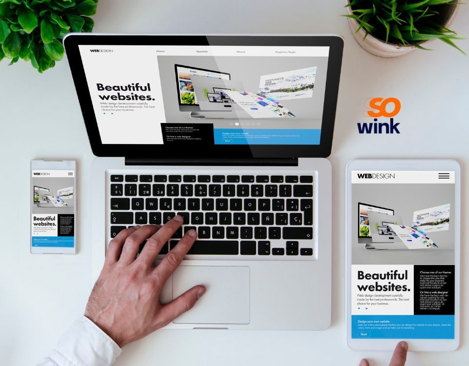 Un ordinateur portable, une tablette et un smartphone affichent le site « so wink » tandis que des mains interagissent avec les appareils sur un bureau.