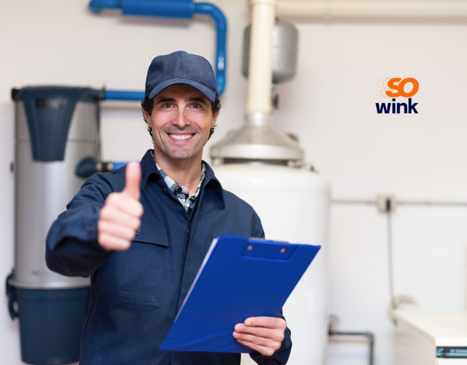 Un technicien en uniforme bleu lève le pouce, tenant un bloc-notes dans un environnement industriel.