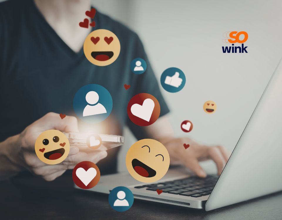 Une personne utilisant un ordinateur portable avec des icônes de réactions de réseaux sociaux, des cœurs et des émojis flottant autour de ses mains.