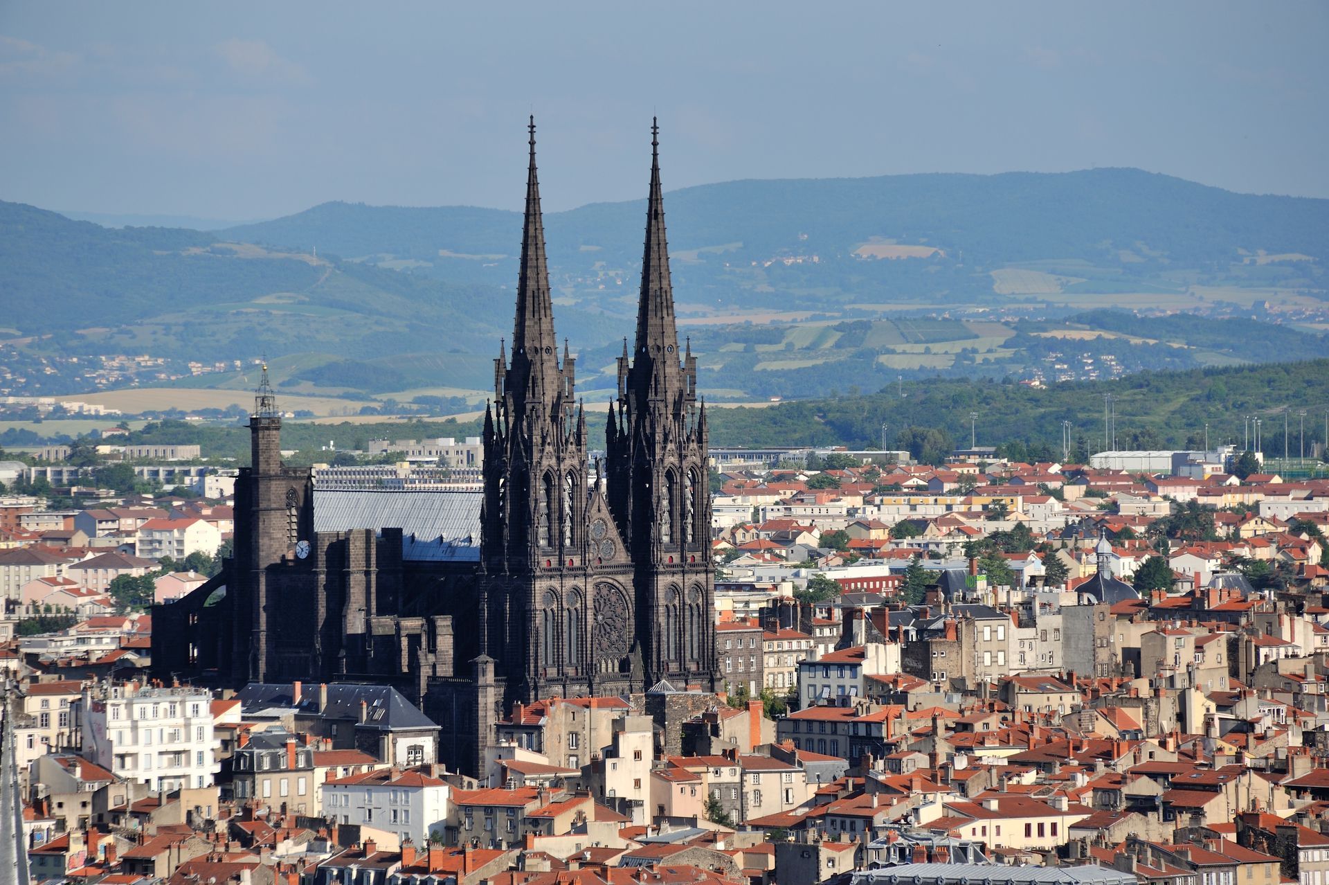 Cathédrale gothique sombre aux flèches jumelles dominant les toits denses de la ville de Clermont-Ferrand, en France.