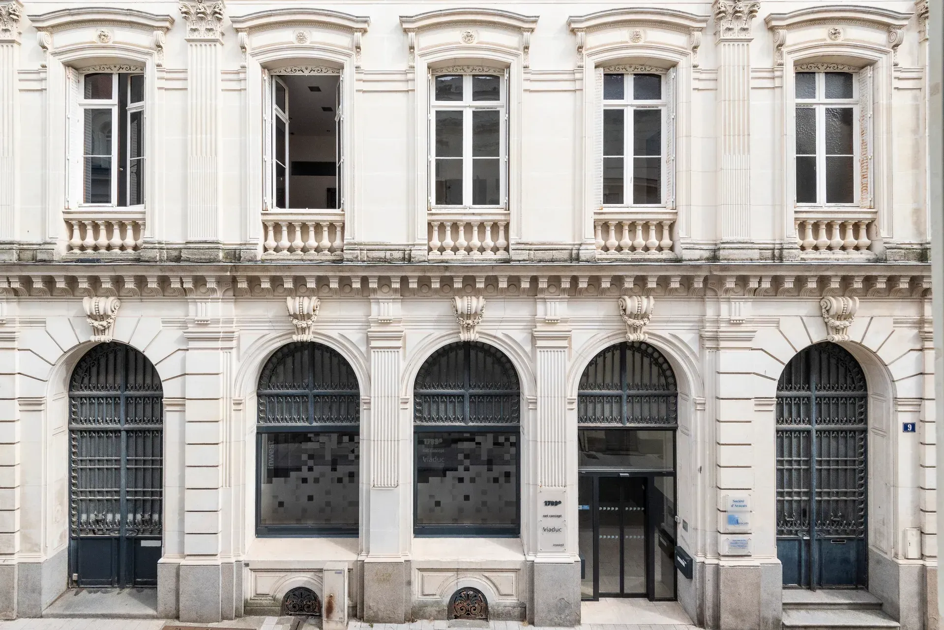 Façade d'immeuble couleur crème avec des fenêtres cintrées au rez-de-chaussée et des fenêtres rectangulaires à l'étage, de style classique.