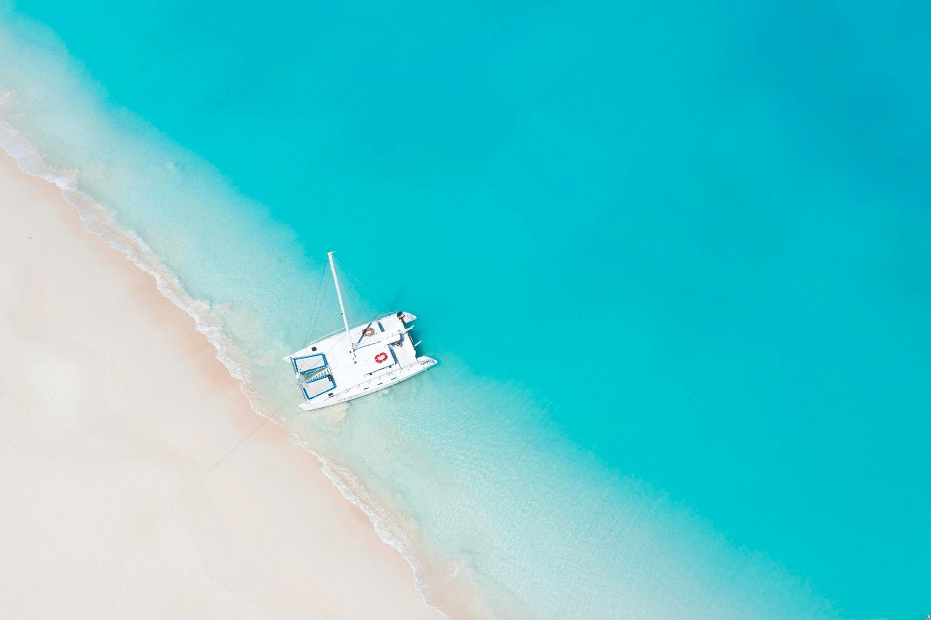 Un catamaran blanc ancré dans des eaux turquoise peu profondes et limpides, le long d'une plage de sable.
