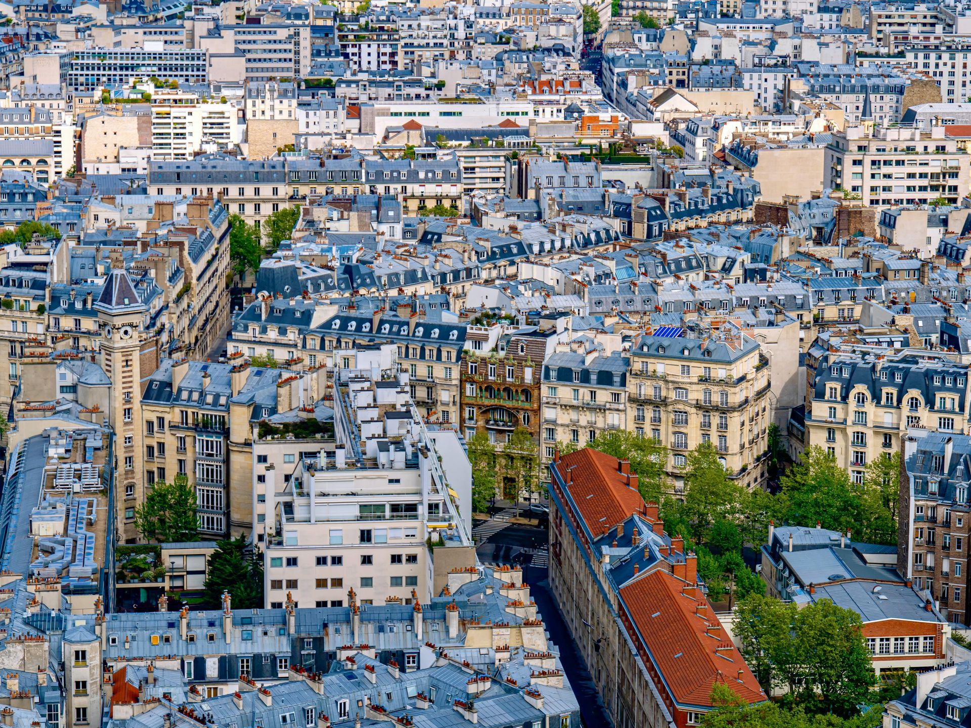 Vue aérienne d'un paysage urbain parisien dense, avec ses immeubles traditionnels aux toits gris et ses îlots de verdure.