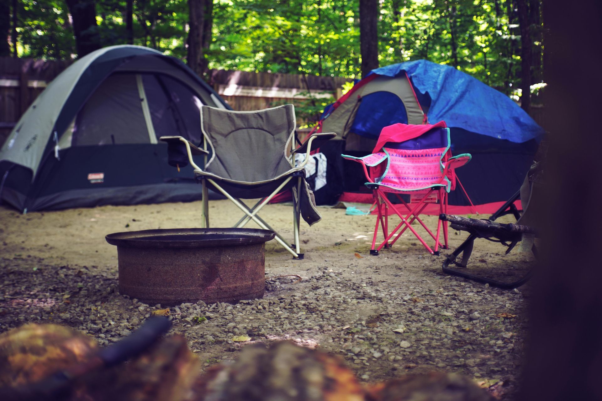 Deux tentes de camping installées dans une zone boisée, avec deux chaises de camping et un foyer au premier plan.
