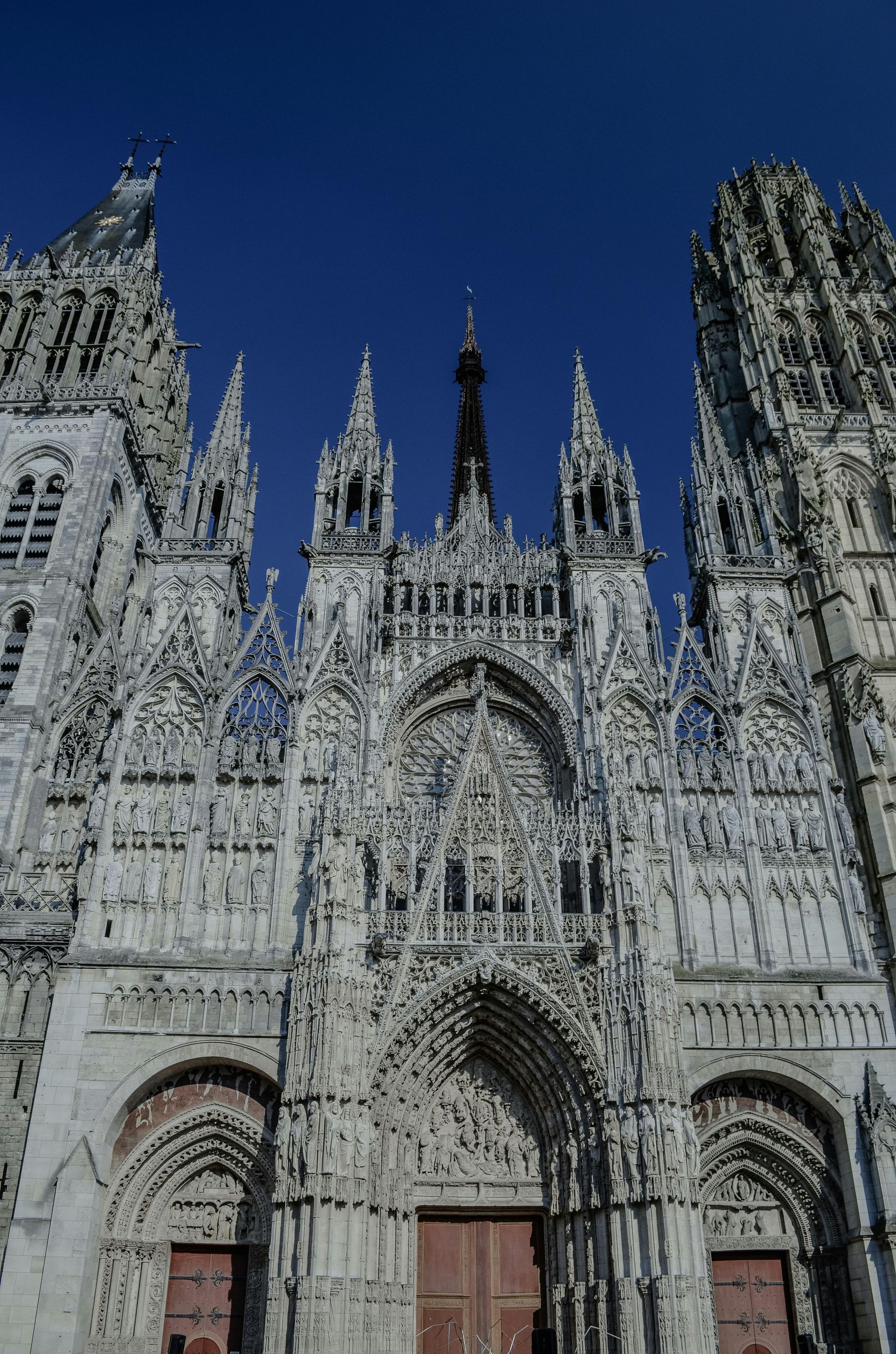 Façade gothique en pierre ornée de la cathédrale de Rouen, avec ses sculptures complexes et ses tours, se détachant sur un ciel bleu clair.