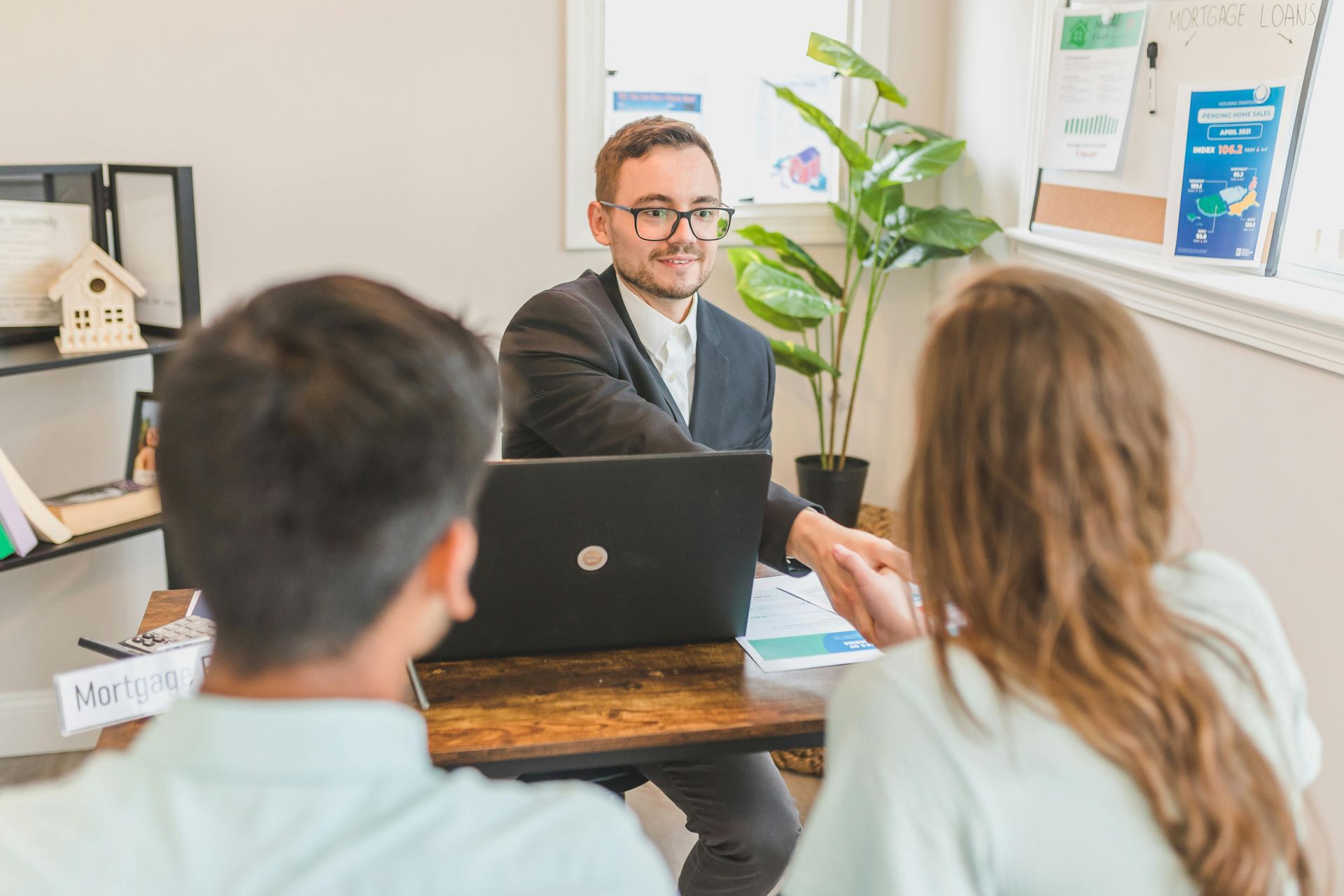 Un professionnel en costume serre la main d'un client de l'autre côté d'un bureau, tandis qu'une autre personne est assise à ses côtés dans un bureau.
