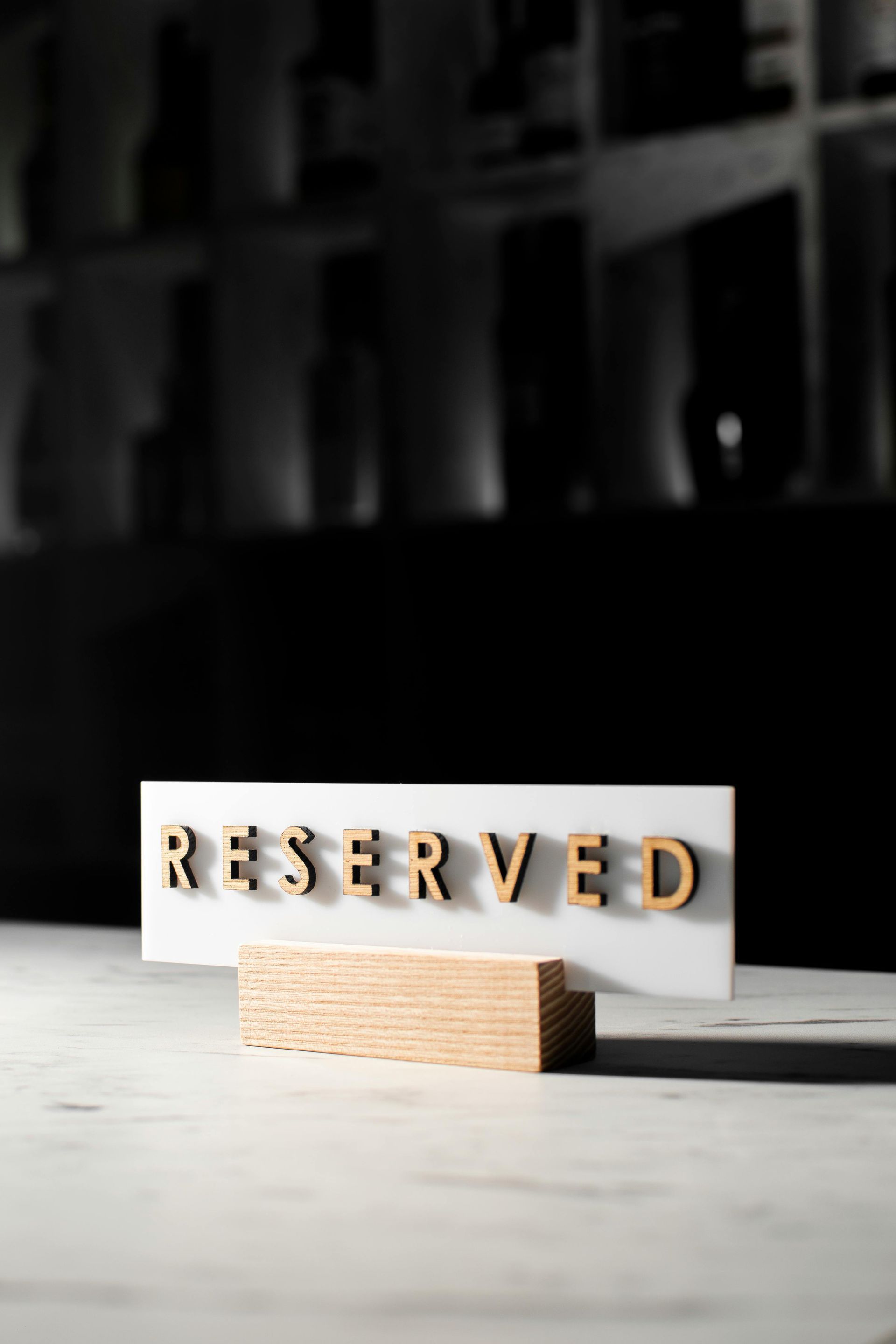 Un panneau rectangulaire blanc « RÉSERVÉ » avec des lettres en bois en relief, posé sur un support en bois sur une surface en marbre blanc.
