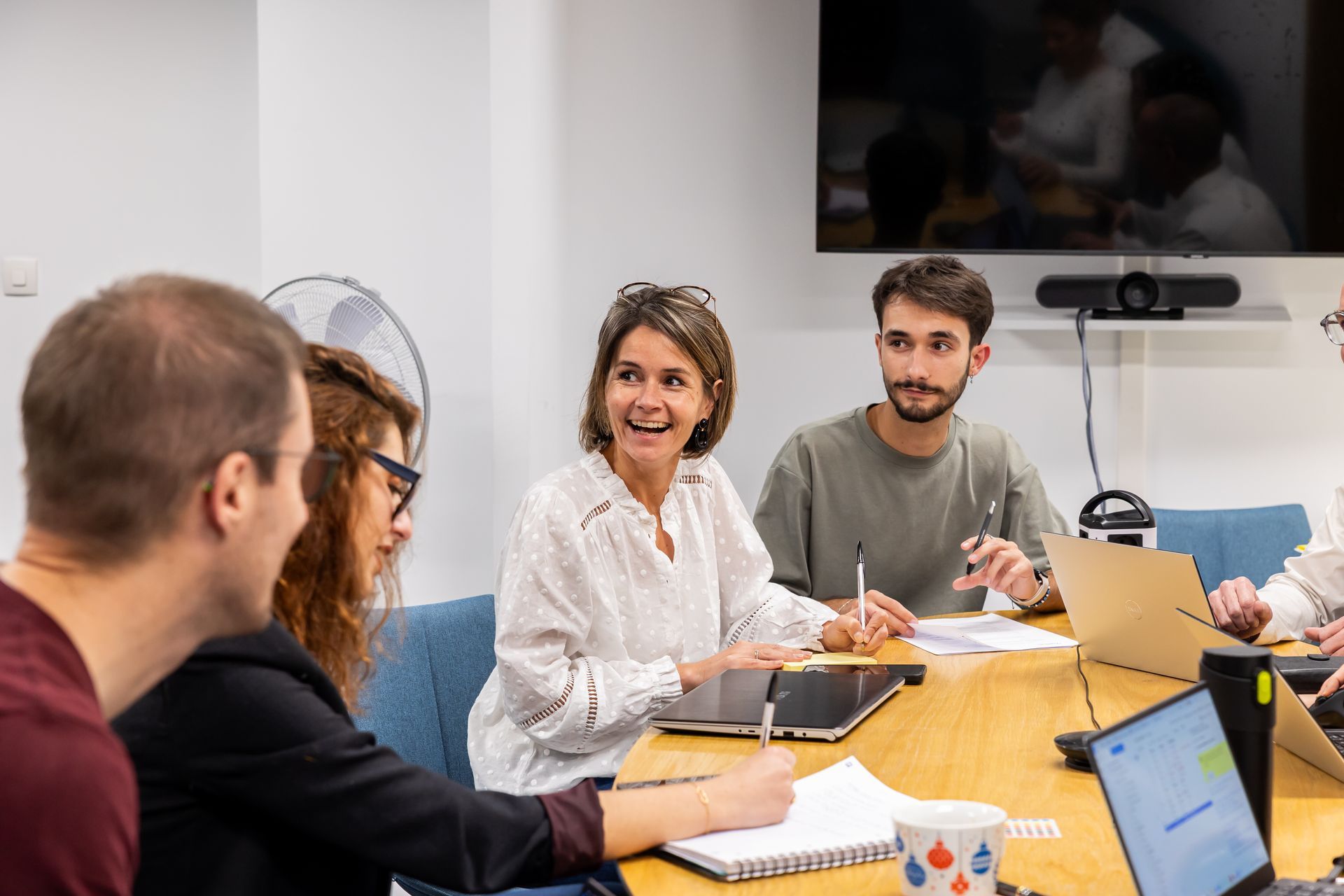 Un groupe de collègues assis autour d'une table en bois dans un bureau, riant et collaborant lors d'une réunion de travail.