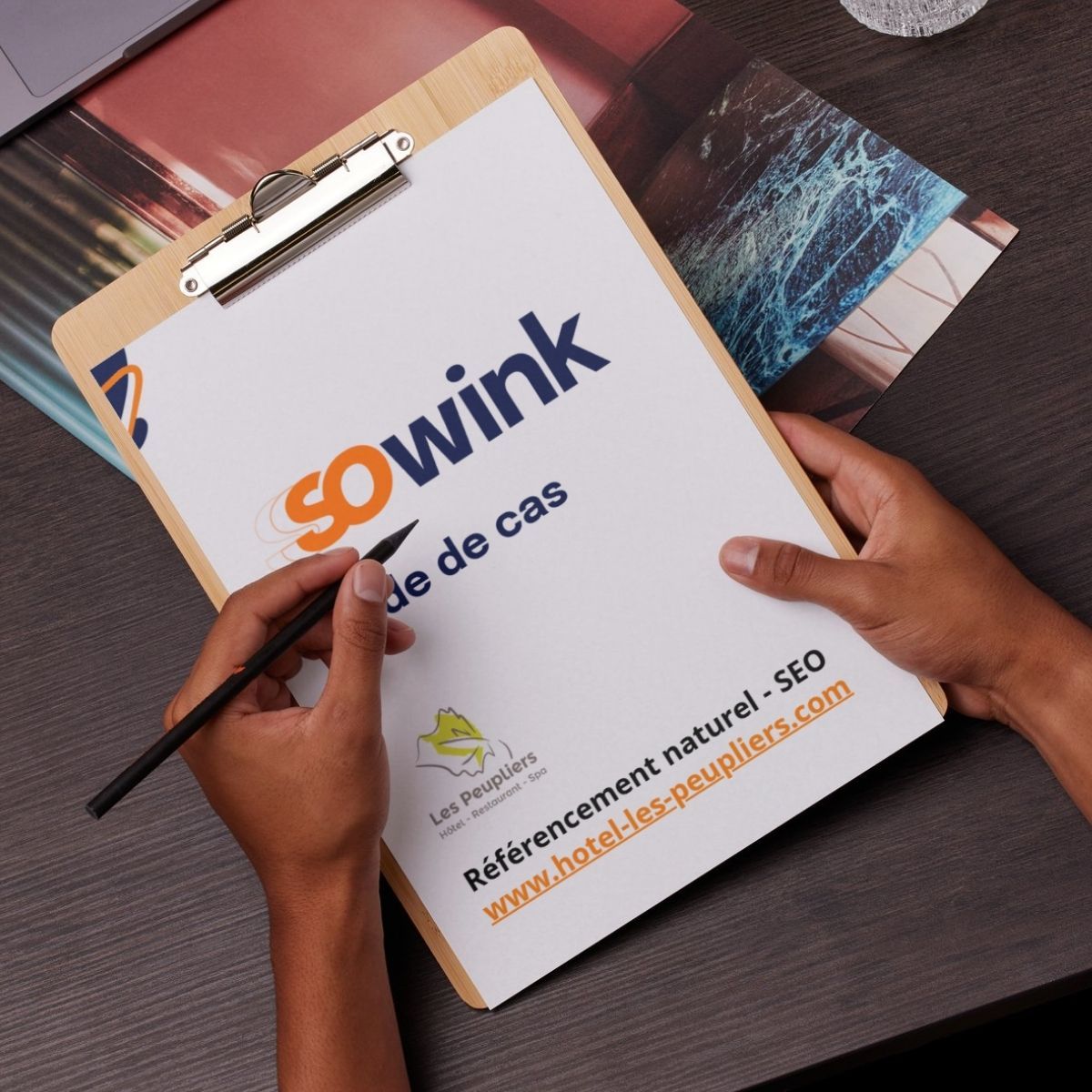Des mains tiennent un bloc-notes avec le logo « sowink », un titre de projet et le texte « hotel-les-peupliers.com » sur un bureau sombre.