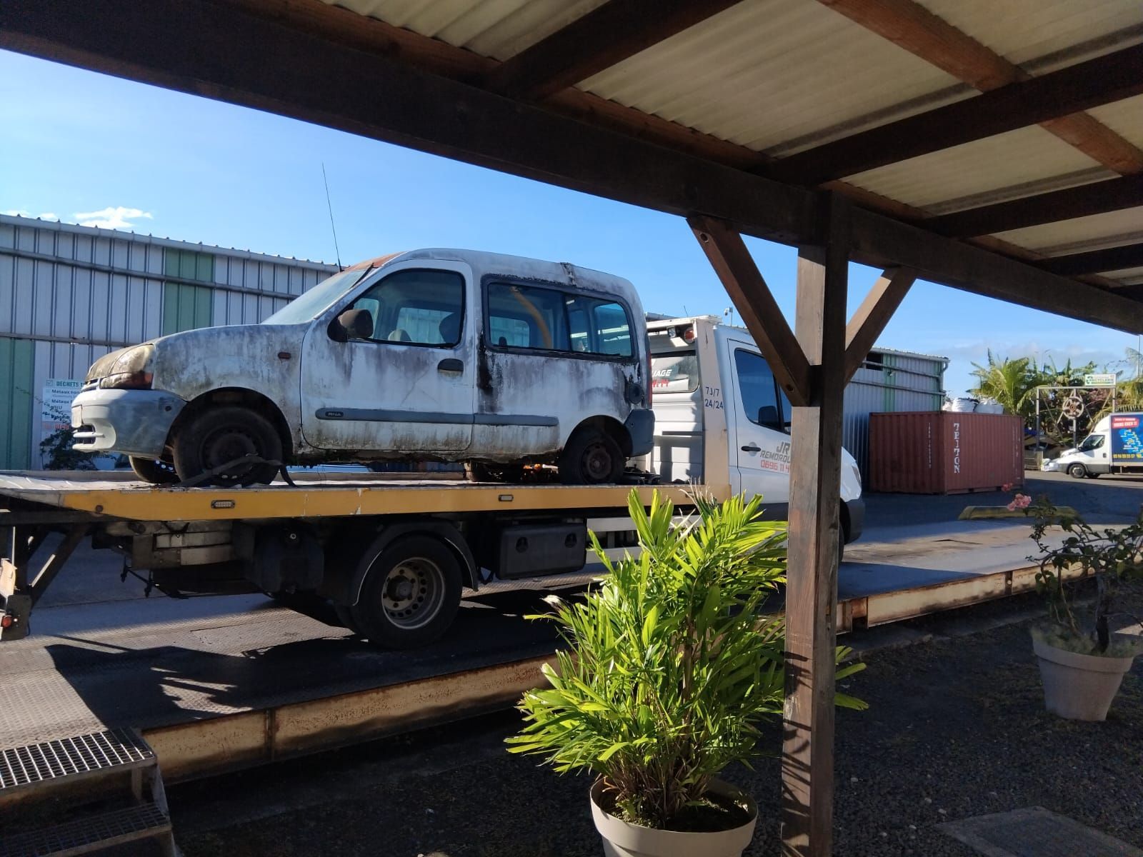 Camion endommagé chargé sur une remorque sous un abri de voiture.