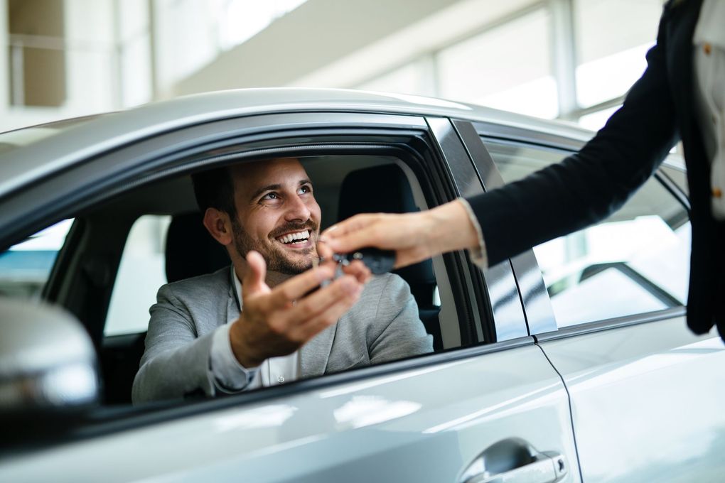 Un conducteur souriant tend les clés par la fenêtre de sa voiture à une personne à l'extérieur.