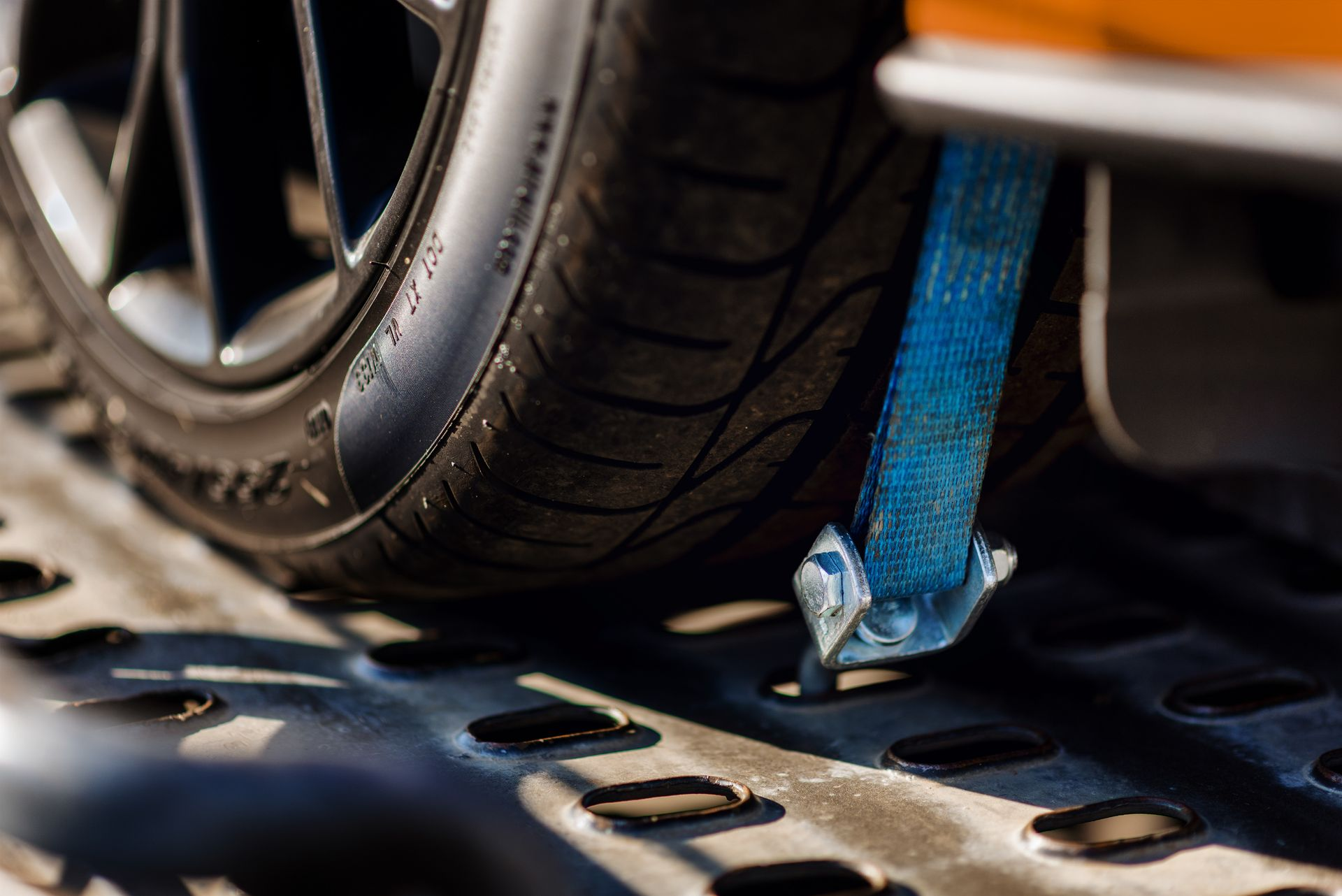 Sangle bleue fixant un pneu de voiture à une plateforme de transport.