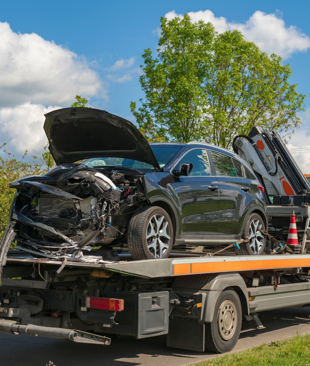 Voiture noire endommagée chargée sur une dépanneuse après une collision, capot ouvert.