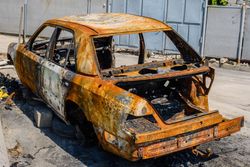 Carrosserie rouillée et calcinée d'une voiture abandonnée sur un terrain vague, dépouillée et carbonisée après un incendie.